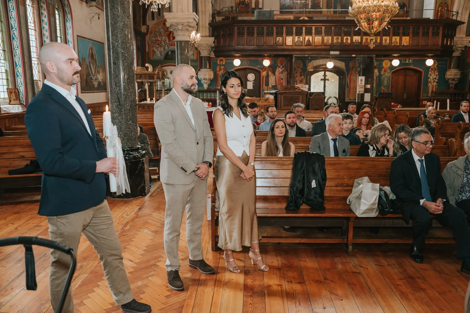  Wide view of St Constantine &amp; St Helen Church in Crystal Palace during a Greek Orthodox christening service with family seated in wooden pews. 