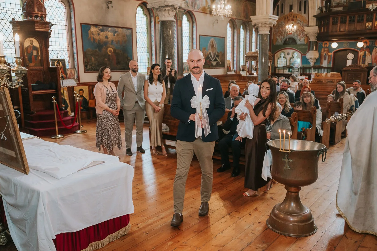  Family and godparents gathered around the baptismal font inside St Constantine &amp; St Helen Church in Crystal Palace. 