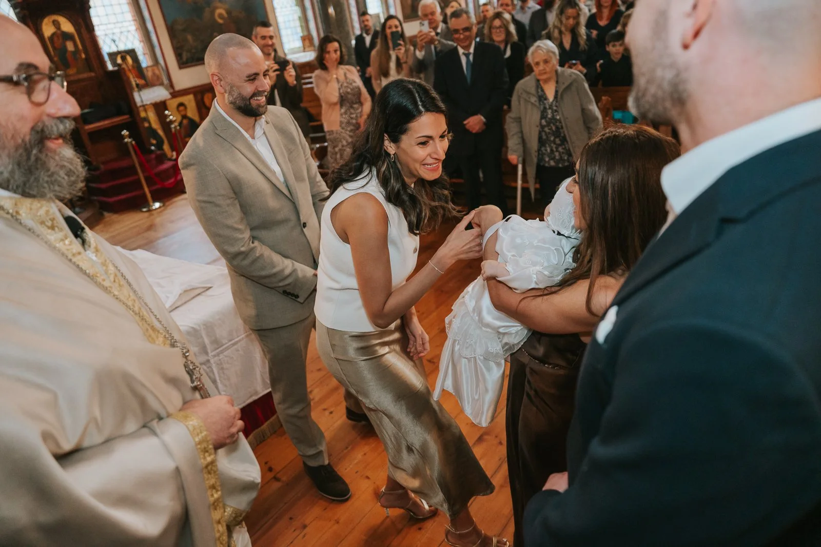  Family smiling and gathering around the baby during a baptism service at St Constantine &amp; St Helen Greek Orthodox Church, South London. 