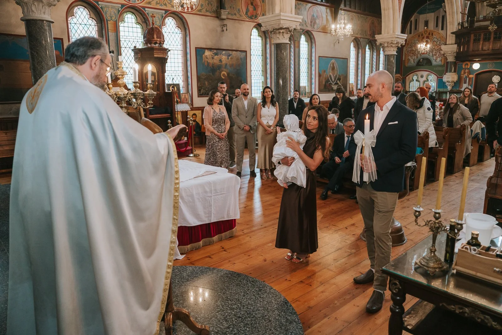  Priest leading a Greek Orthodox christening ceremony at St Constantine &amp; St Helen Church in Crystal Palace, with parents and godfather standing before the congregation. 