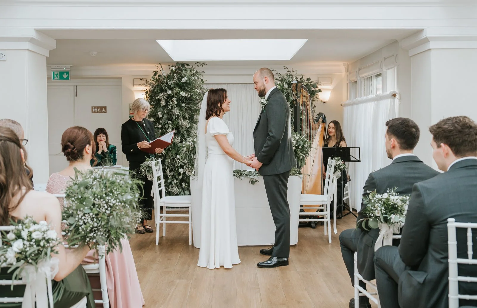  Bride and groom exchanging vows during their ceremony in the Belvedere Suite at Pembroke Lodge, bright conservatory wedding venue in Richmond Park. 