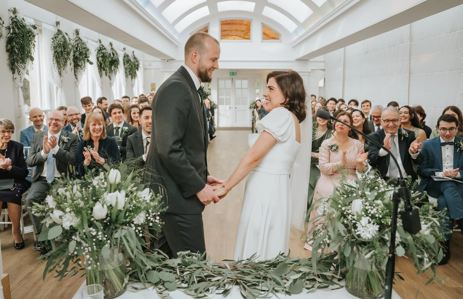  Bride and groom smiling at each other after exchanging vows in the Belvedere Suite at Pembroke Lodge, elegant Richmond Park civil wedding ceremony. 