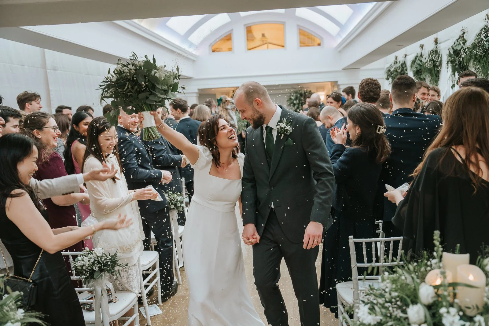  Bride and groom celebrating with confetti after their ceremony in the Belvedere Suite at Pembroke Lodge, joyful Richmond Park wedding moment. 