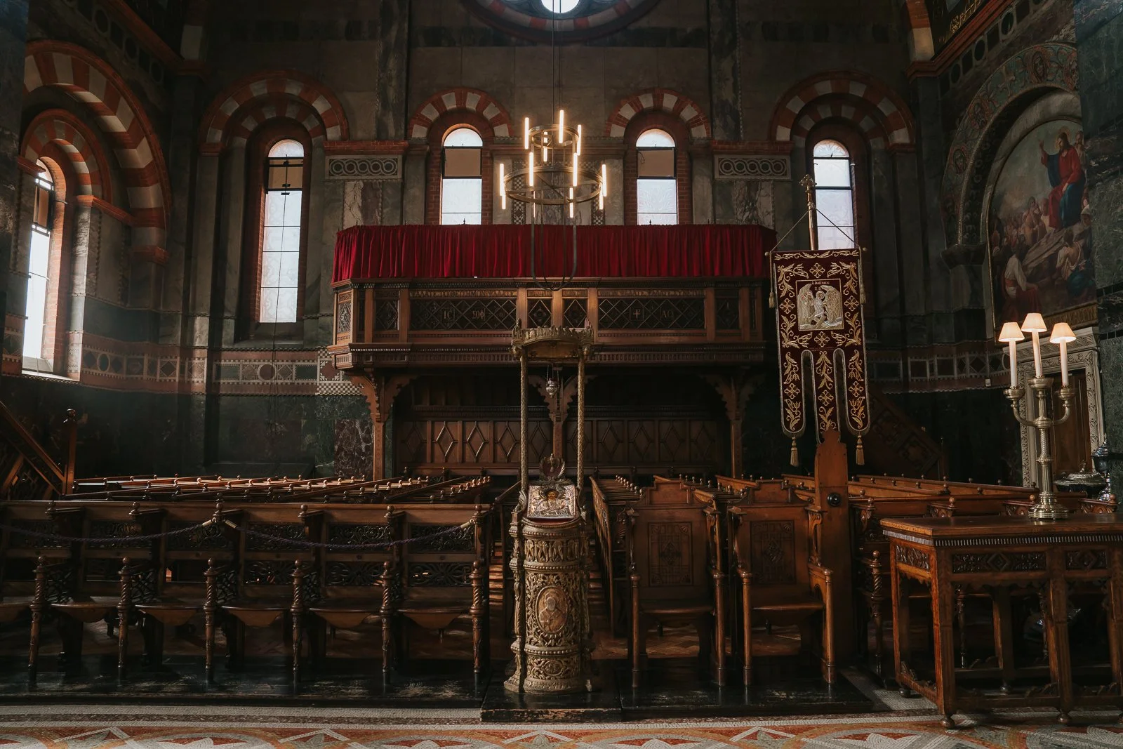  Wide interior view of Saint Sofia Greek Orthodox Cathedral London with wooden pews, chandeliers and natural light streaming through arched windows 