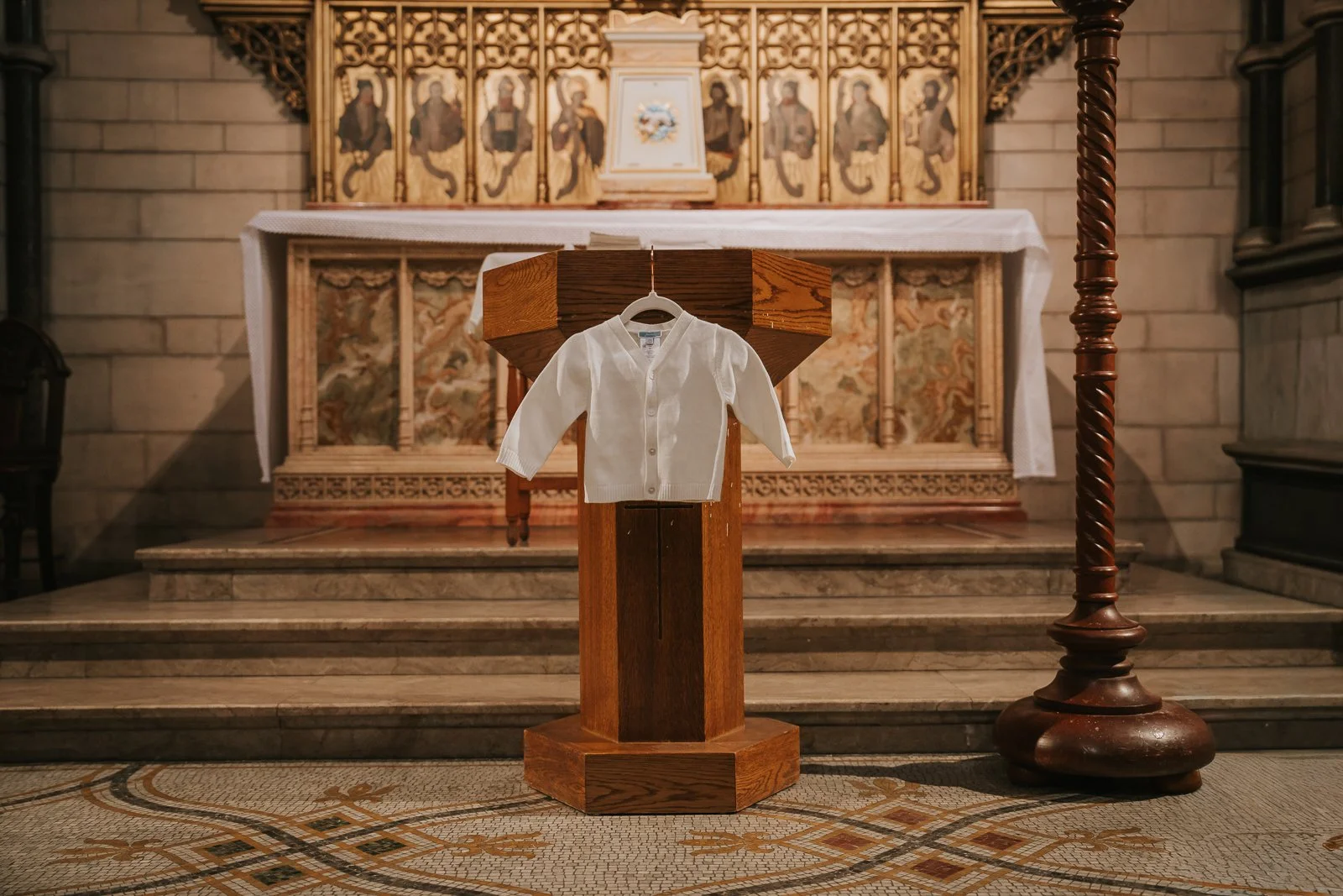  Baby’s white christening cardigan displayed on lectern inside St James’ Catholic Church Spanish Place London. 