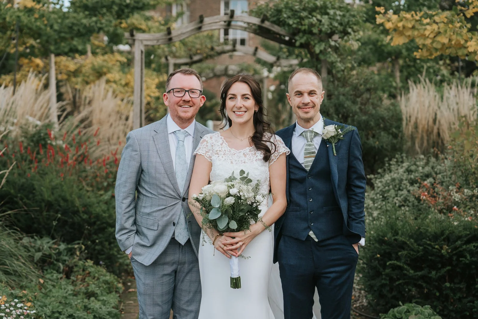  Bride and groom with guest portrait in Morden Park House gardens, elegant South London wedding venue with greenery backdrop, natural wedding photography style 