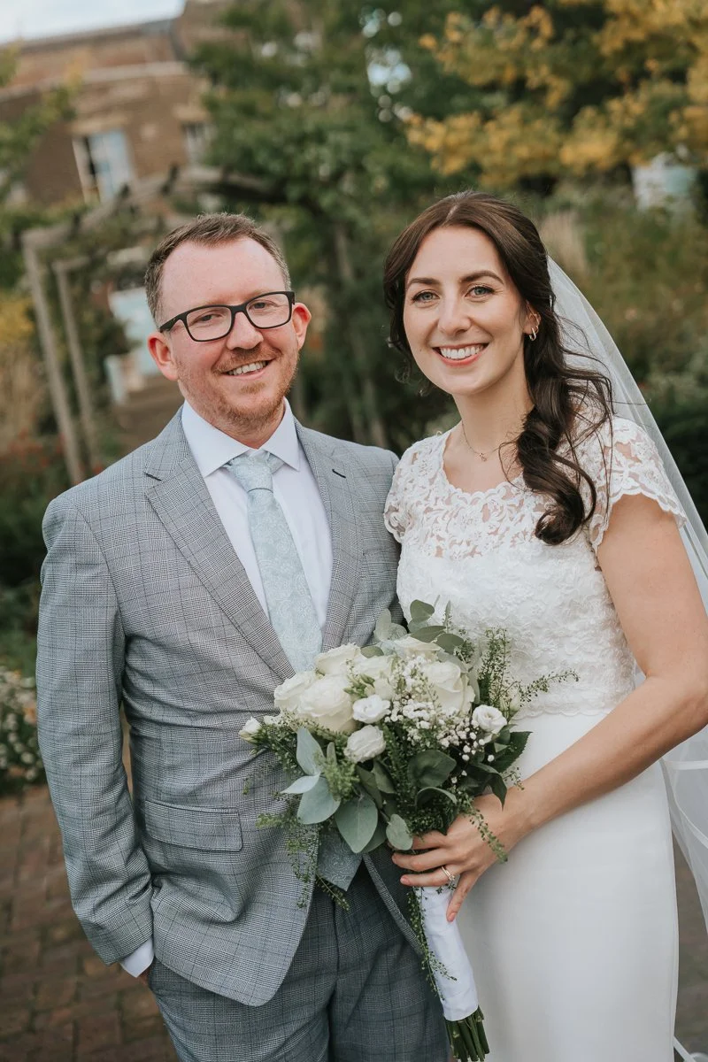  Bride holding bouquet with guest at Morden Park House wedding, soft natural light, relaxed London wedding photographer capturing candid moments in garden setting 