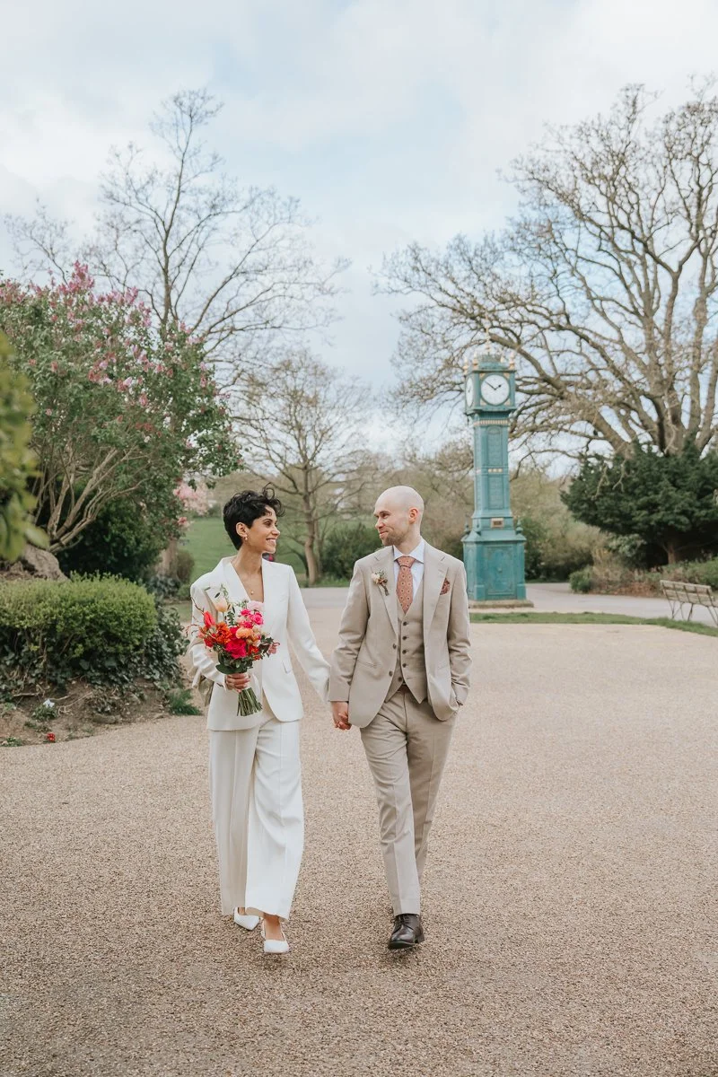  Bride and groom walking past iconic Brockwell Park clock tower, next to wedding venue Brockwell Hall. 