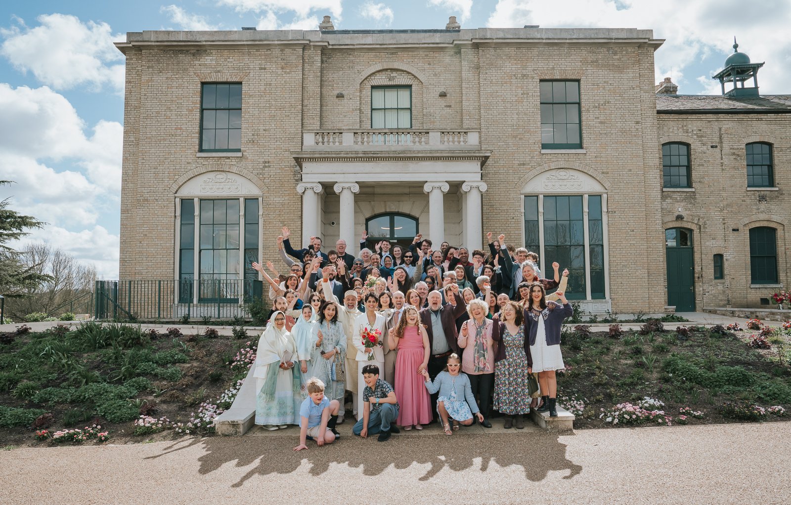  Wedding guests gathered outside Brockwell Hall in Brockwell Park, joyful group photo at South London wedding venue with historic Georgian backdrop. 