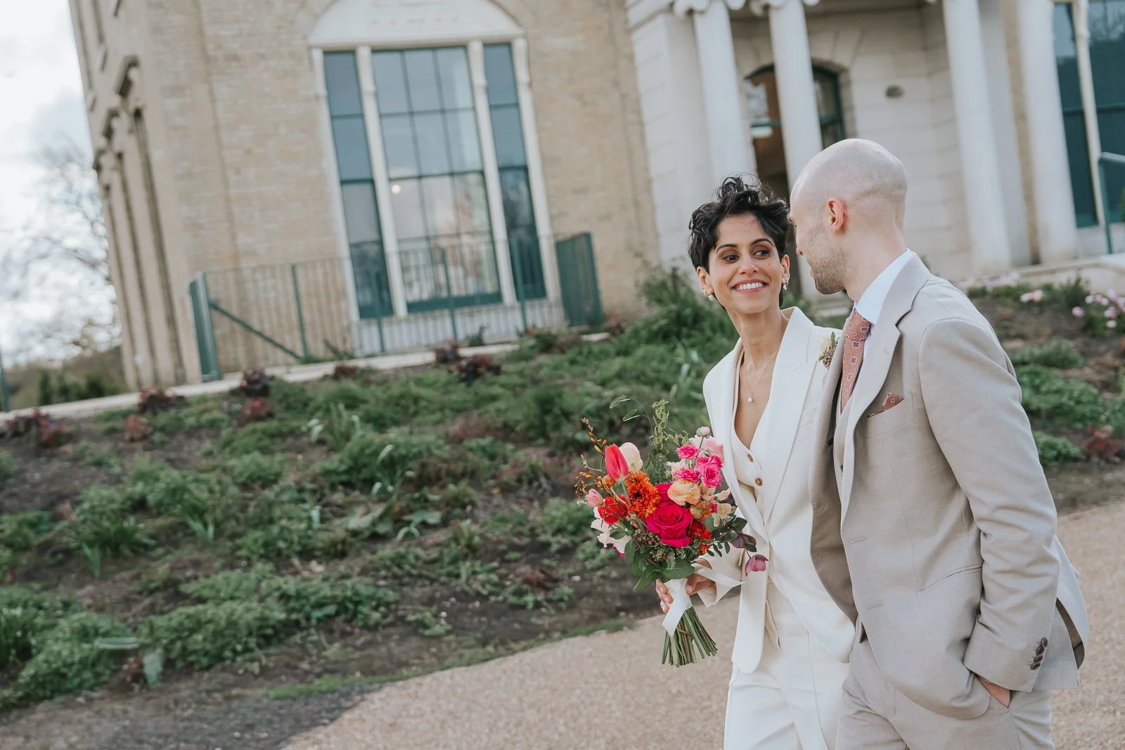  Candid close-up of bride and groom walking together at Brockwell Hall, colourful bouquet and relaxed documentary wedding photography in Brockwell Park. 