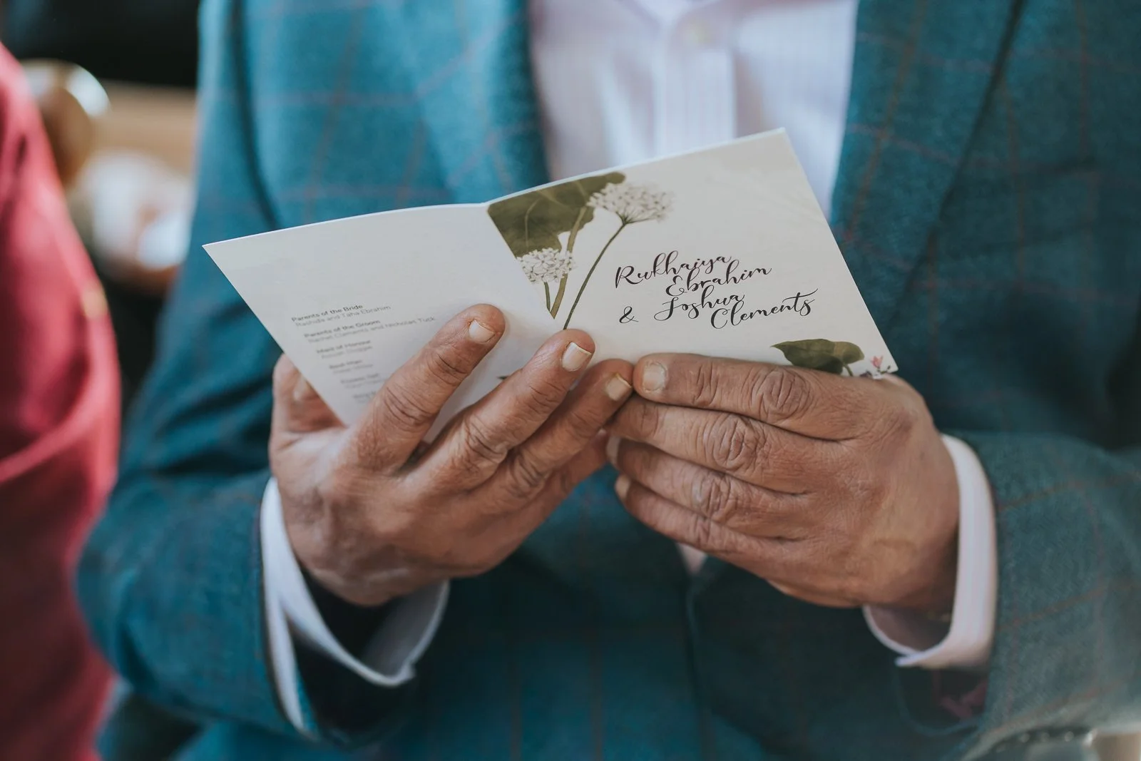  Guest holding wedding order of service booklet at Brockwell Hall, close-up ceremony detail at South London wedding venue. 