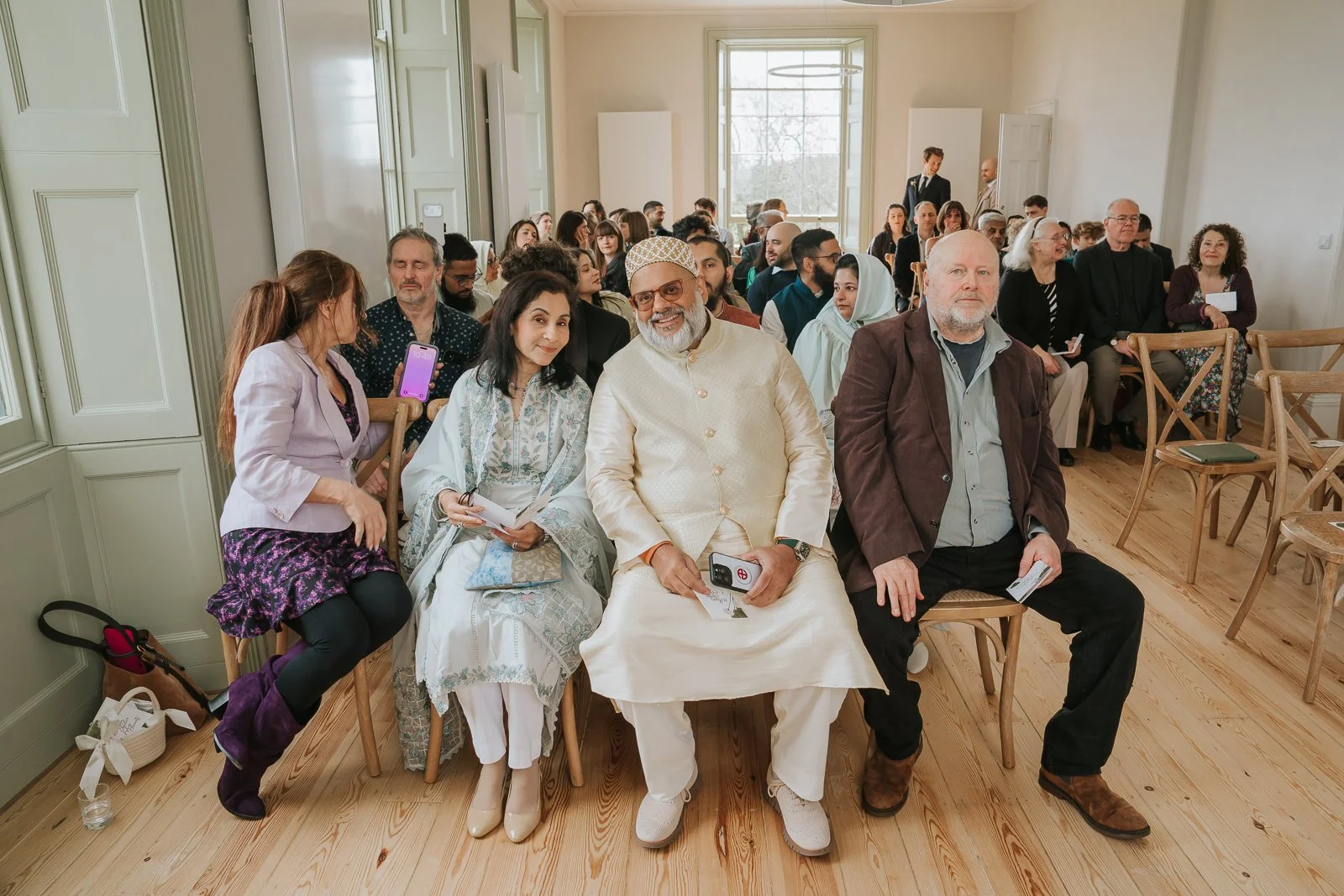  Wedding guests seated inside Brockwell Hall ceremony room, intimate civil wedding in Brockwell Park South London. 