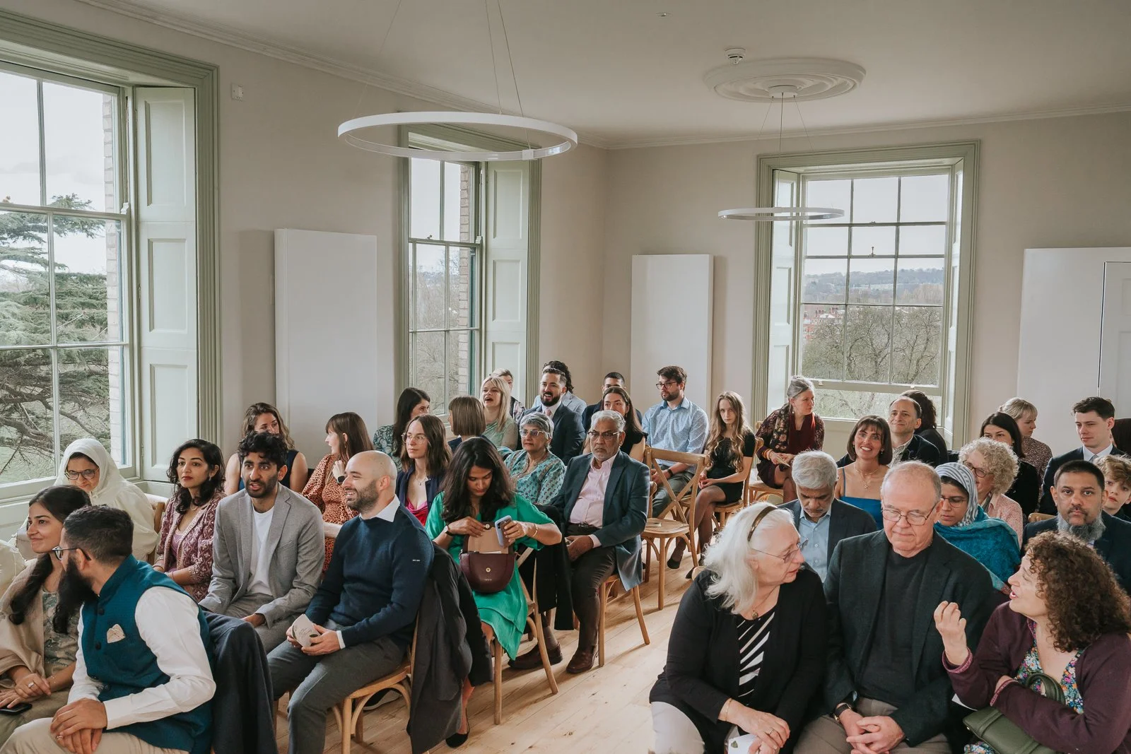  Wide view of Brockwell Hall ceremony room filled with guests, bright natural light and elegant interiors at South London wedding venue. 