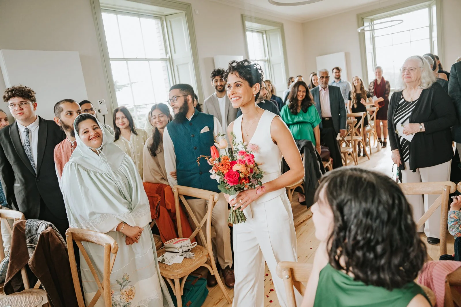  Bride walking down aisle at Brockwell Hall surrounded by smiling guests, emotional indoor ceremony at Brockwell Park wedding venue. 