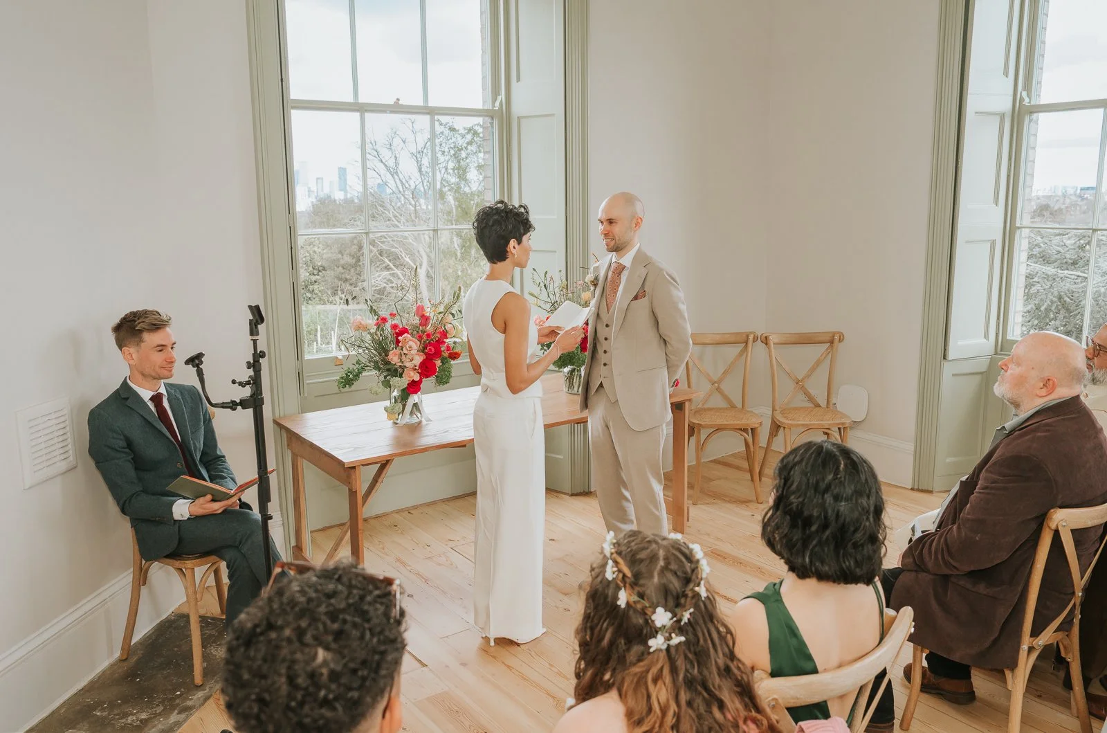  Bride and groom exchanging vows at Brockwell Hall with large windows and London skyline views, Brockwell Park wedding ceremony. 