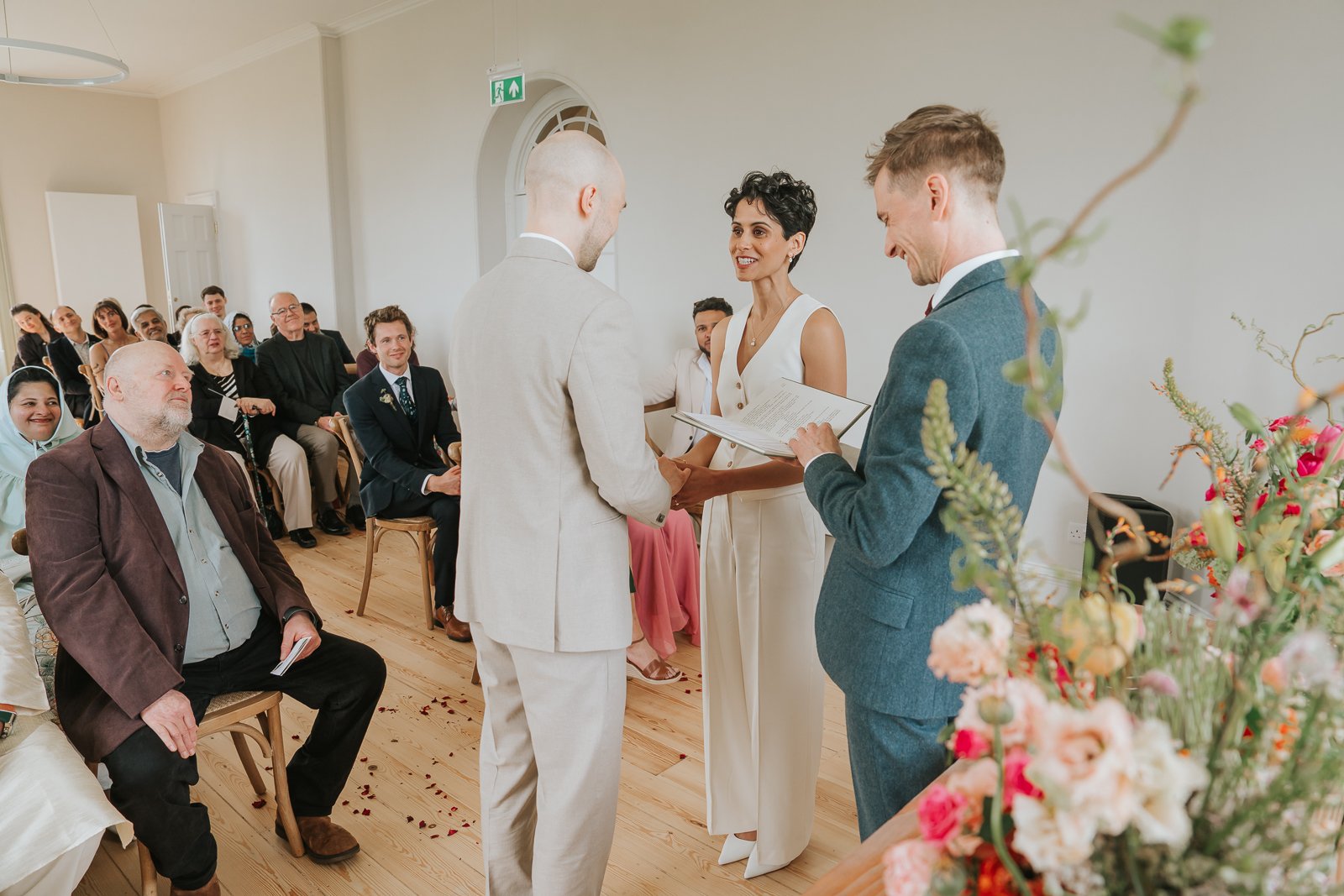  Wedding ceremony at Brockwell Hall with guests watching as couple exchange vows and rings, light-filled South London venue. 