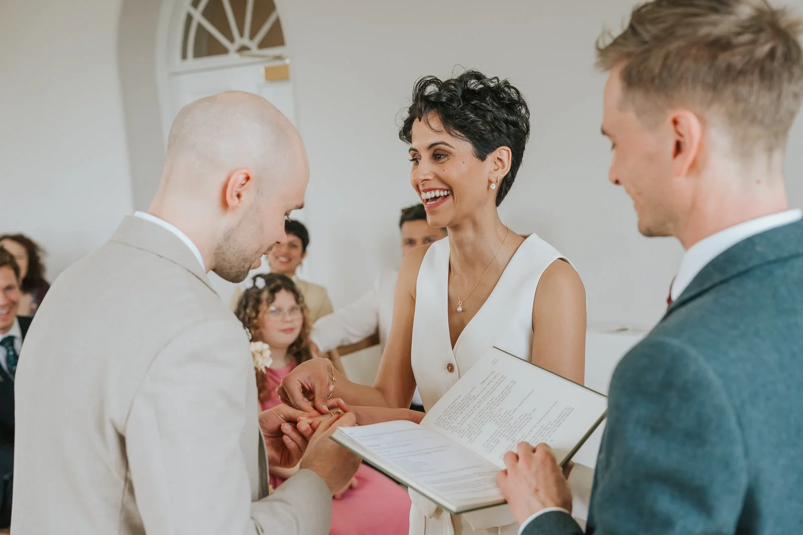  Smiling bride placing wedding ring on groom’s finger during Brockwell Hall ceremony. 