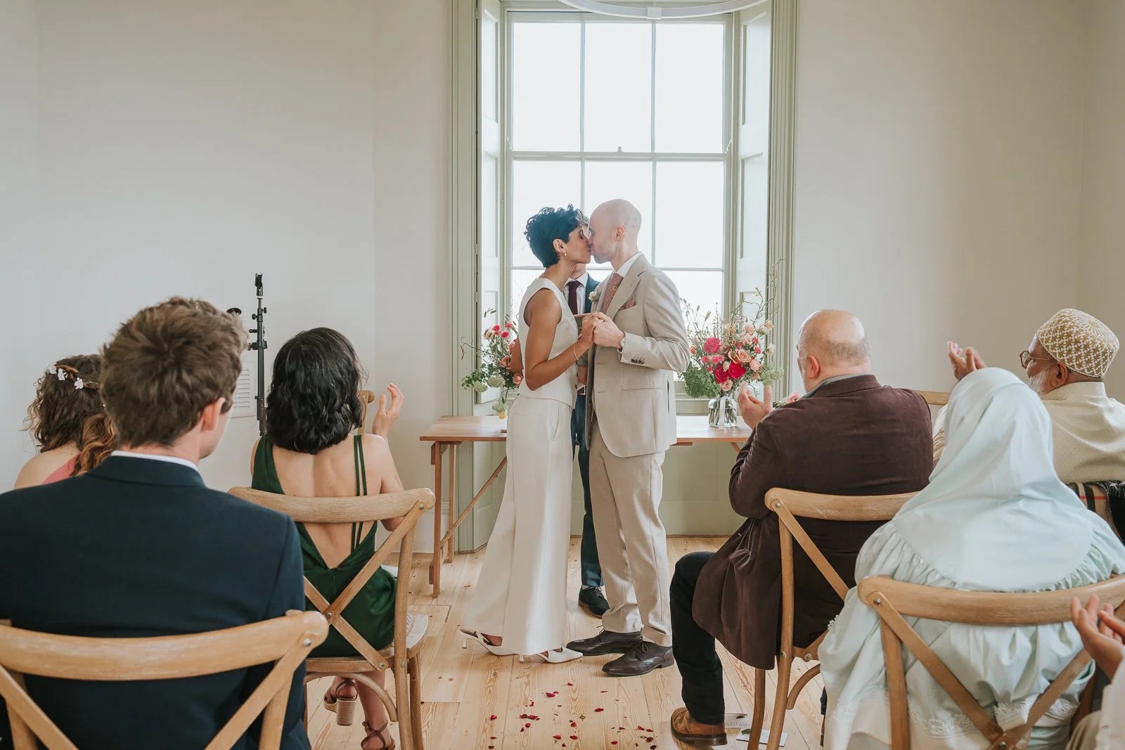  Couple sharing their first kiss at Brockwell Hall wedding ceremony as guests applaud. 