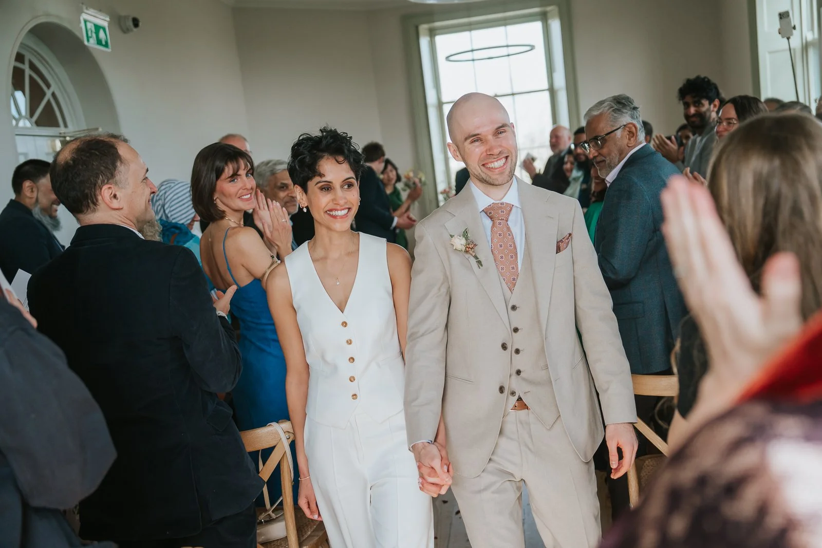  Bride and groom walking down the aisle after Brockwell Hall ceremony as guests applaud, joyful South London wedding moment. 