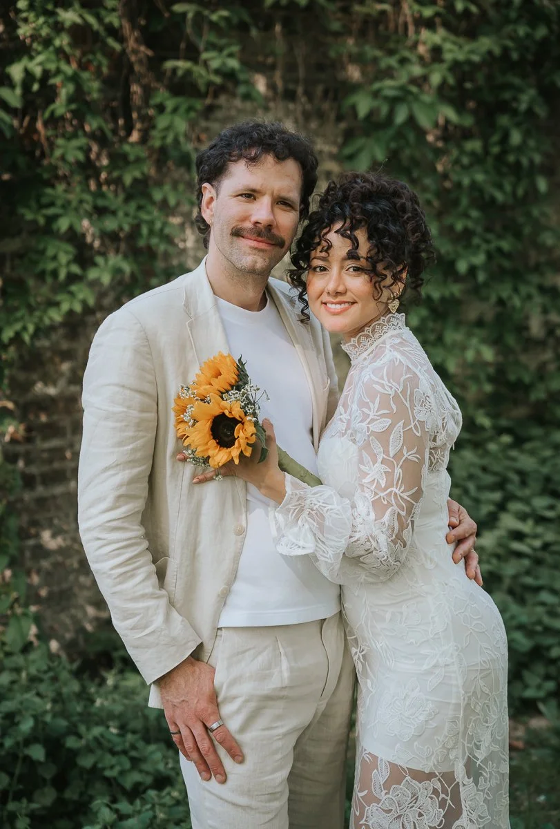  Bride and groom portrait with sunflower bouquet against green ivy wall at Tower Hamlets Registry Office wedding.   