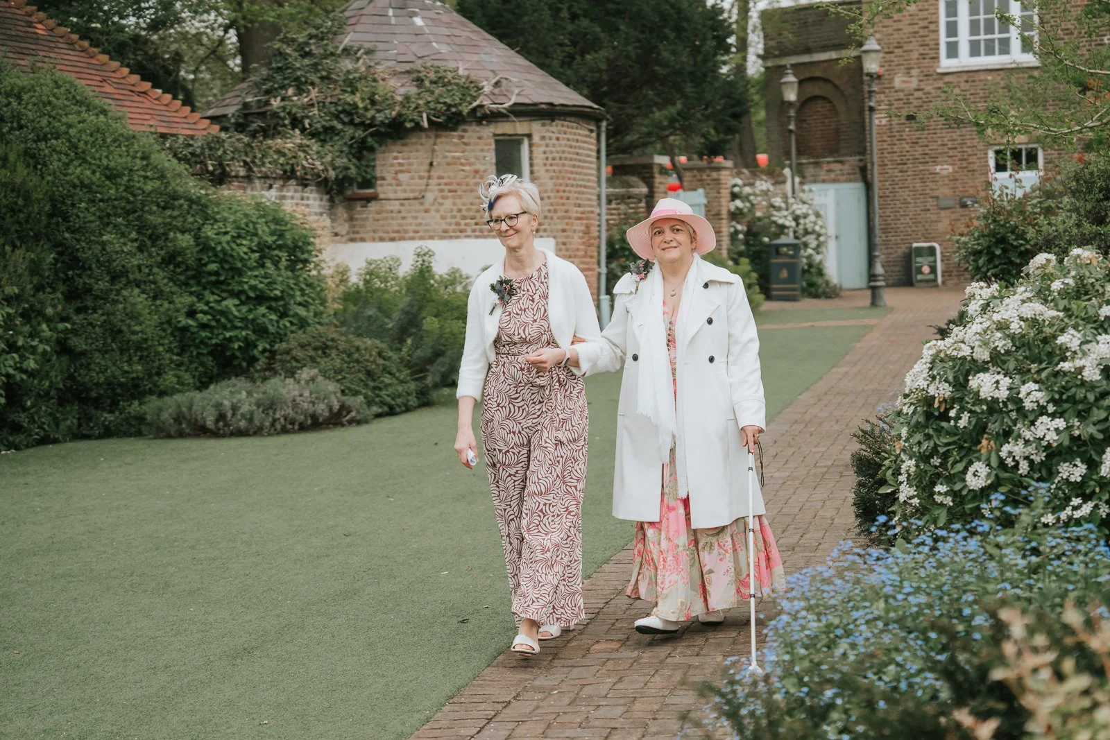  Wedding guests arriving through the gardens at Morden Park House before the ceremony, with landscaped pathways and historic Georgian buildings in the background. 