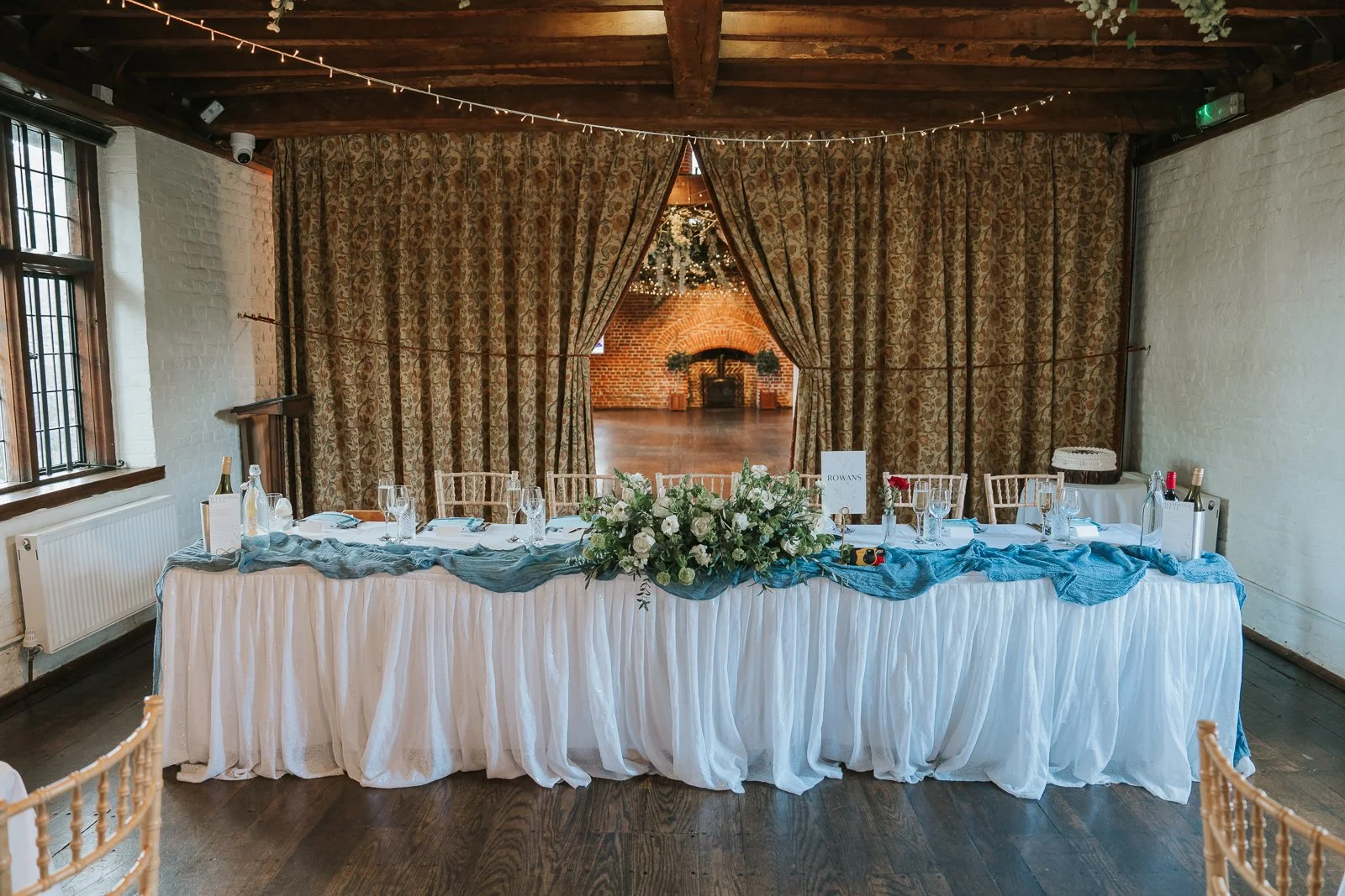  Elegant wedding reception top table inside Tudor Barn Eltham with floral centrepieces, fairy lights, exposed wooden beams and rustic Tudor barn interiors. 