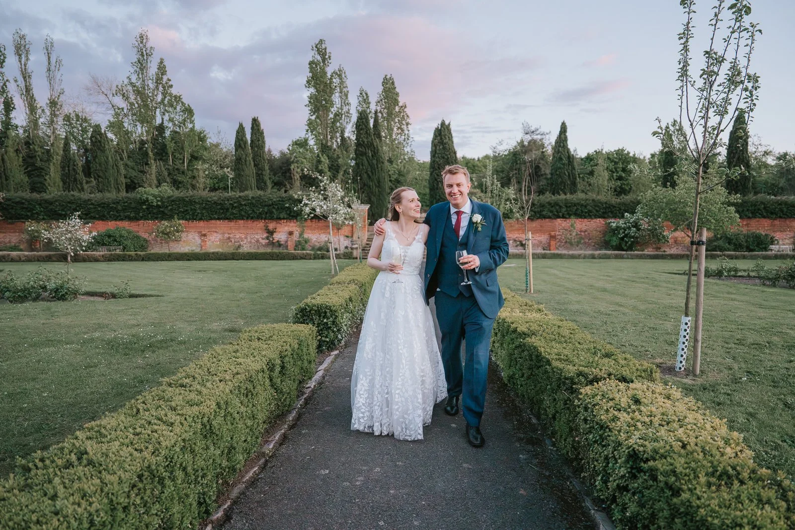  Bride and groom enjoying a relaxed walk through the gardens at Tudor Barn Eltham with spring flowers, manicured grounds and romantic evening light. 