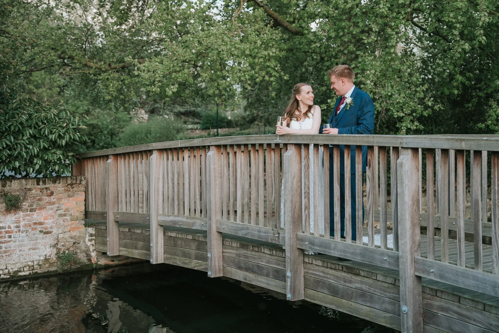  Bride and groom sharing a quiet moment on the wooden bridge in the gardens at Tudor Barn Eltham during their wedding portraits. 