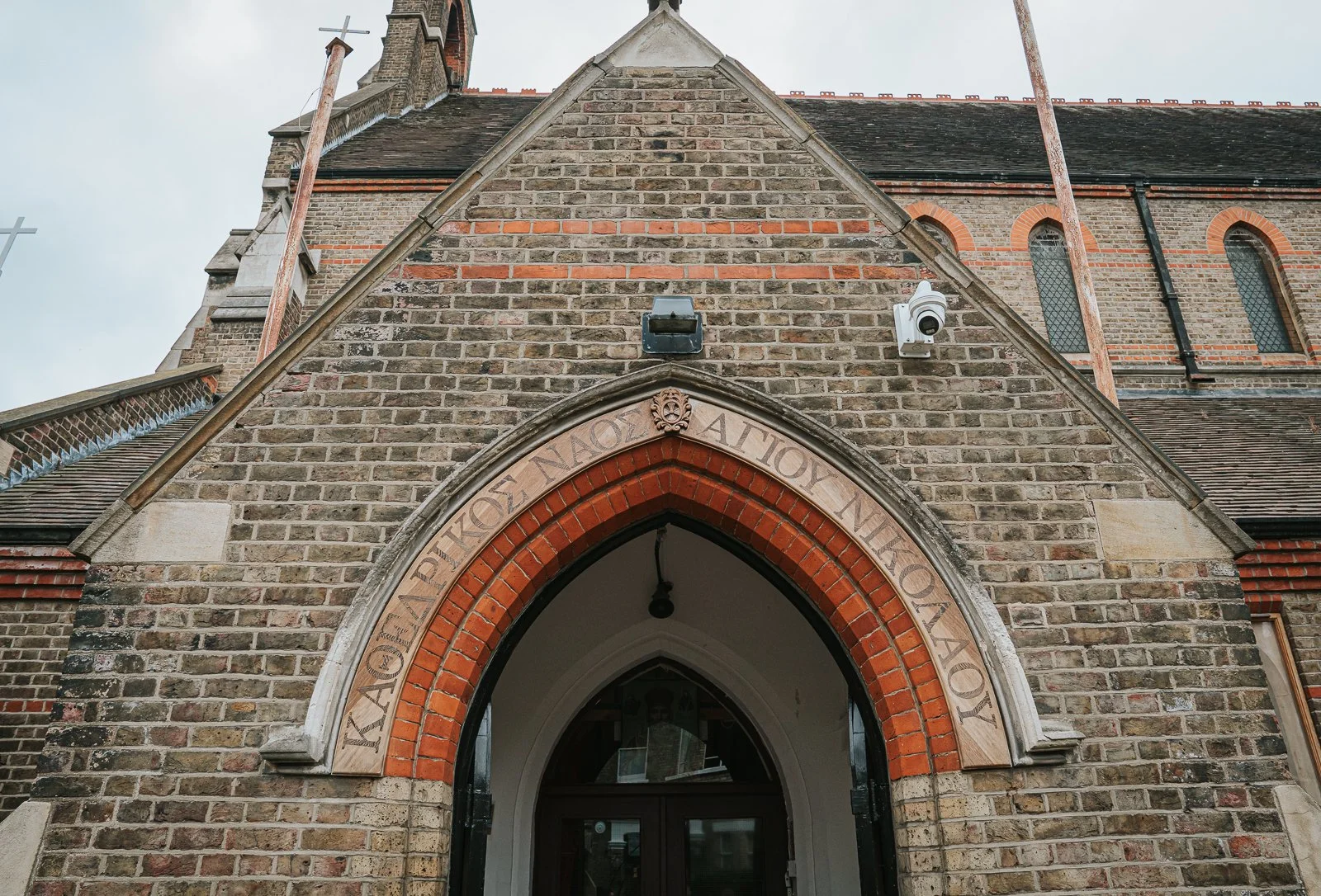  Close-up of the entrance arch at St Nicholas Greek Orthodox Church in Shepherd’s Bush, featuring Greek lettering above the doorway. 