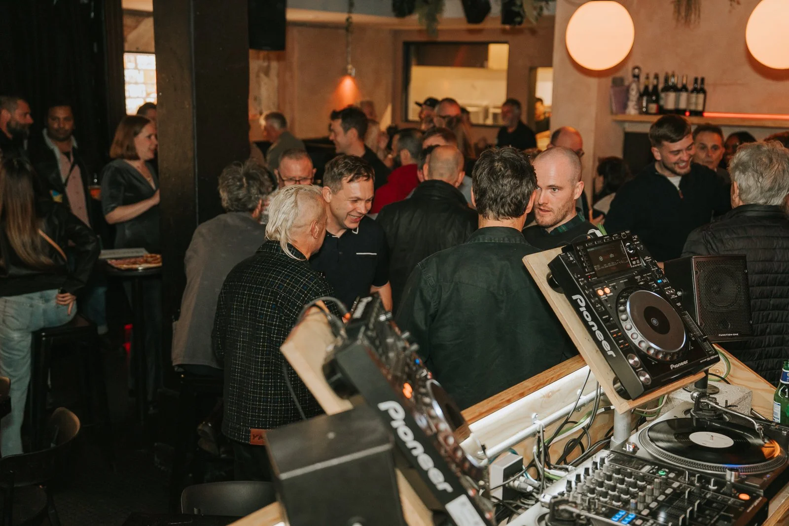  Guests mingling and chatting beside the DJ booth at a lively birthday party venue in Brixton, photographed by a South London event photographer. 