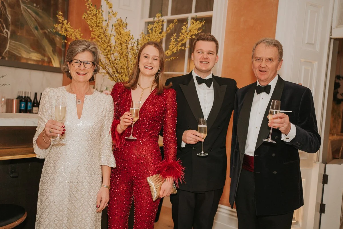  Family members dressed for a milestone birthday celebration, enjoying drinks and posing for a group photograph. 