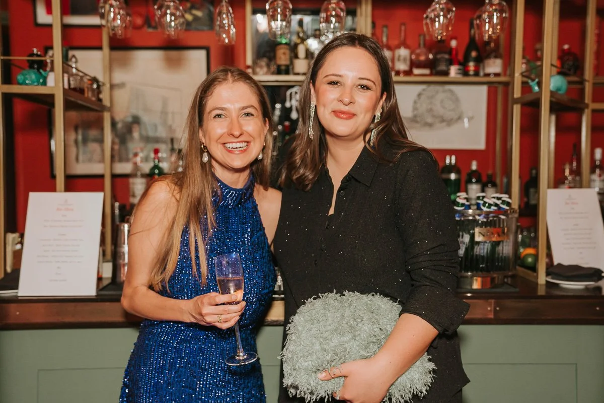  Two friends posing with drinks at a 30th birthday celebration in a trendy bar, captured with natural birthday party photography. 