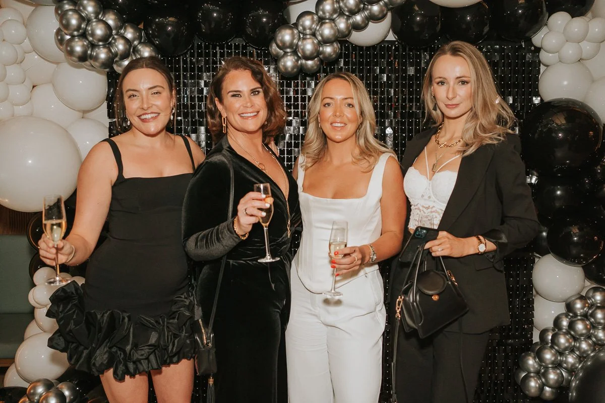  Guests posing beneath a black, white and silver balloon display at a glamorous 30th birthday party in London. 