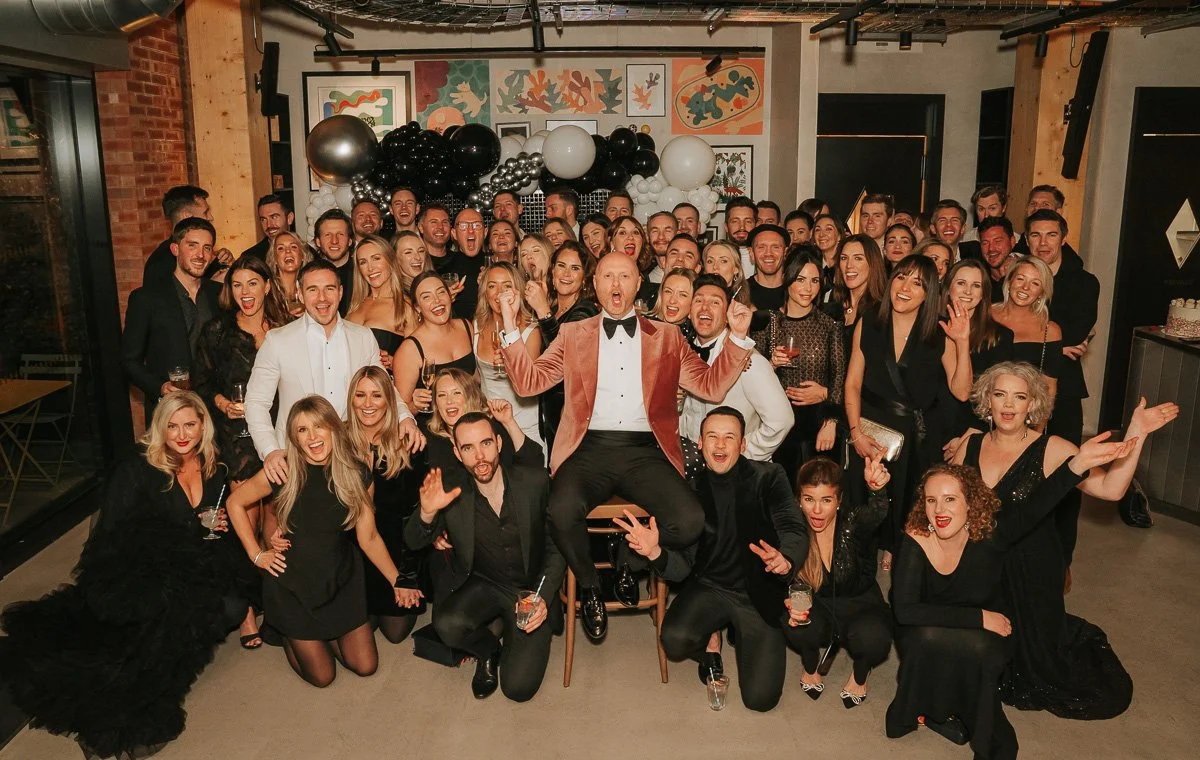  Large group photo of guests celebrating a milestone 40th birthday party at a modern South London event space. 
