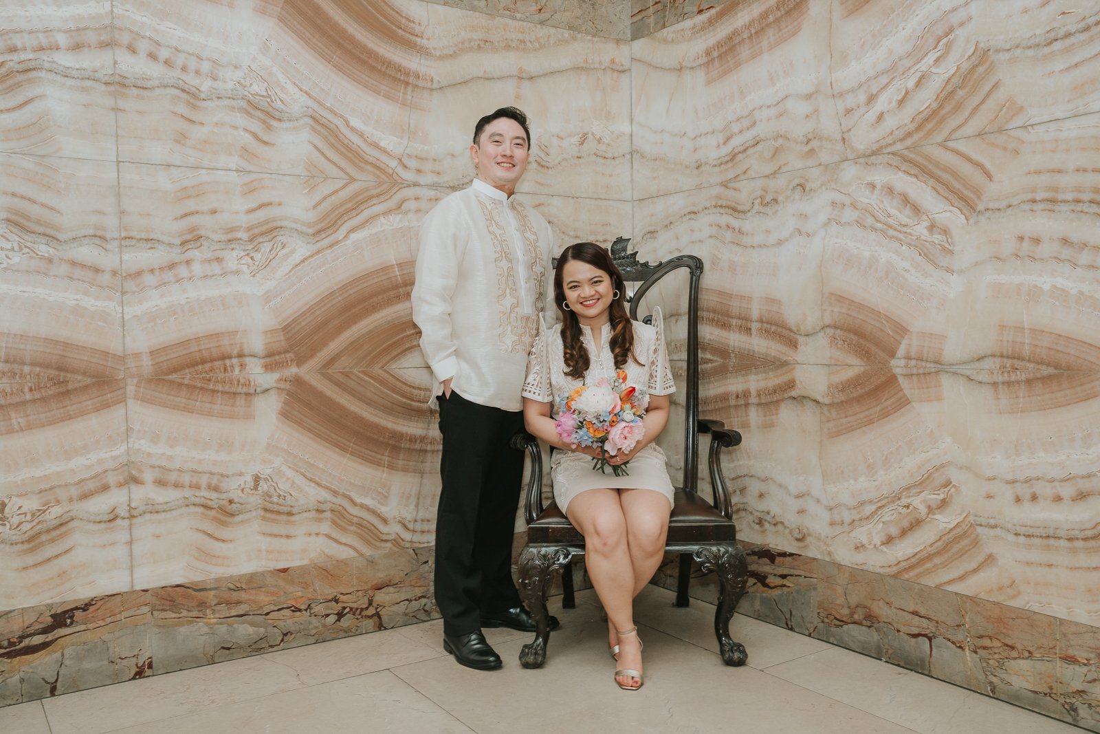  Bride and groom posing with a colourful bouquet against the striking marble walls of Wandsworth Town Hall, a beautiful backdrop for London wedding photography. 