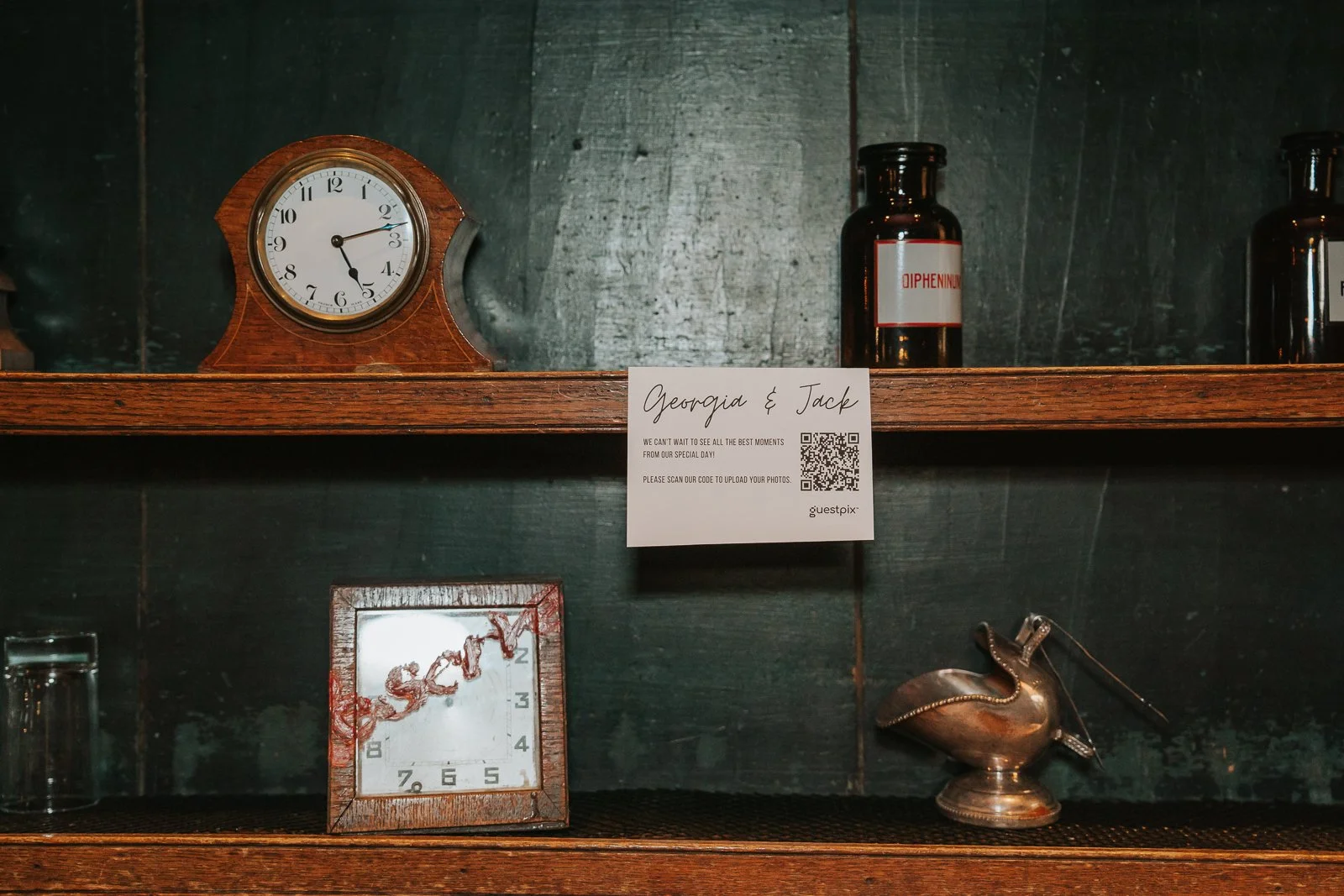  Wedding guest photo-sharing sign displayed on antique wooden shelving with vintage clocks and curiosities at The Zetter Townhouse Clerkenwell. 