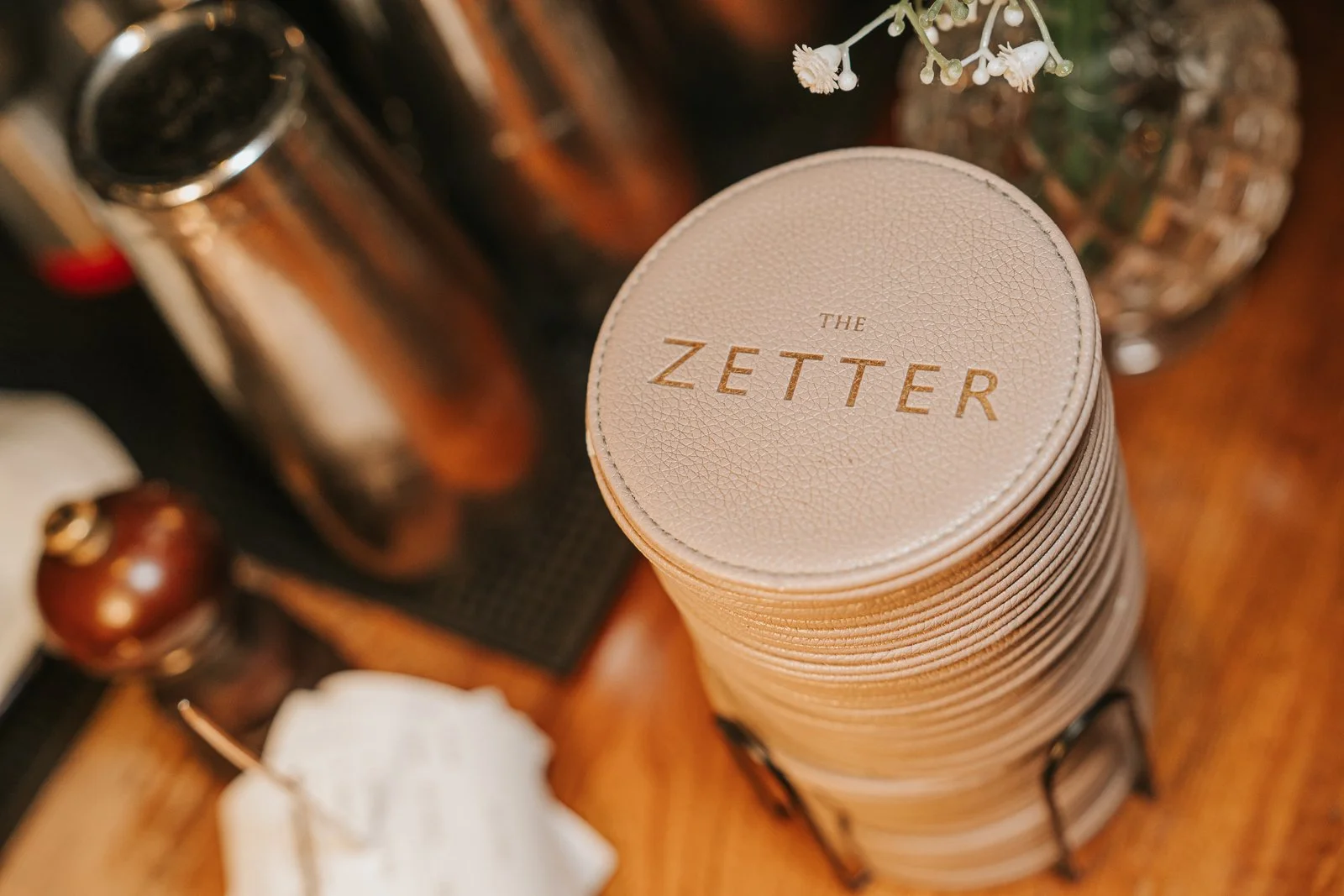  Stack of branded leather-look drinks coasters displayed on a wooden bar at The Zetter Townhouse Clerkenwell, showcasing the venue's stylish and characterful wedding reception décor. 