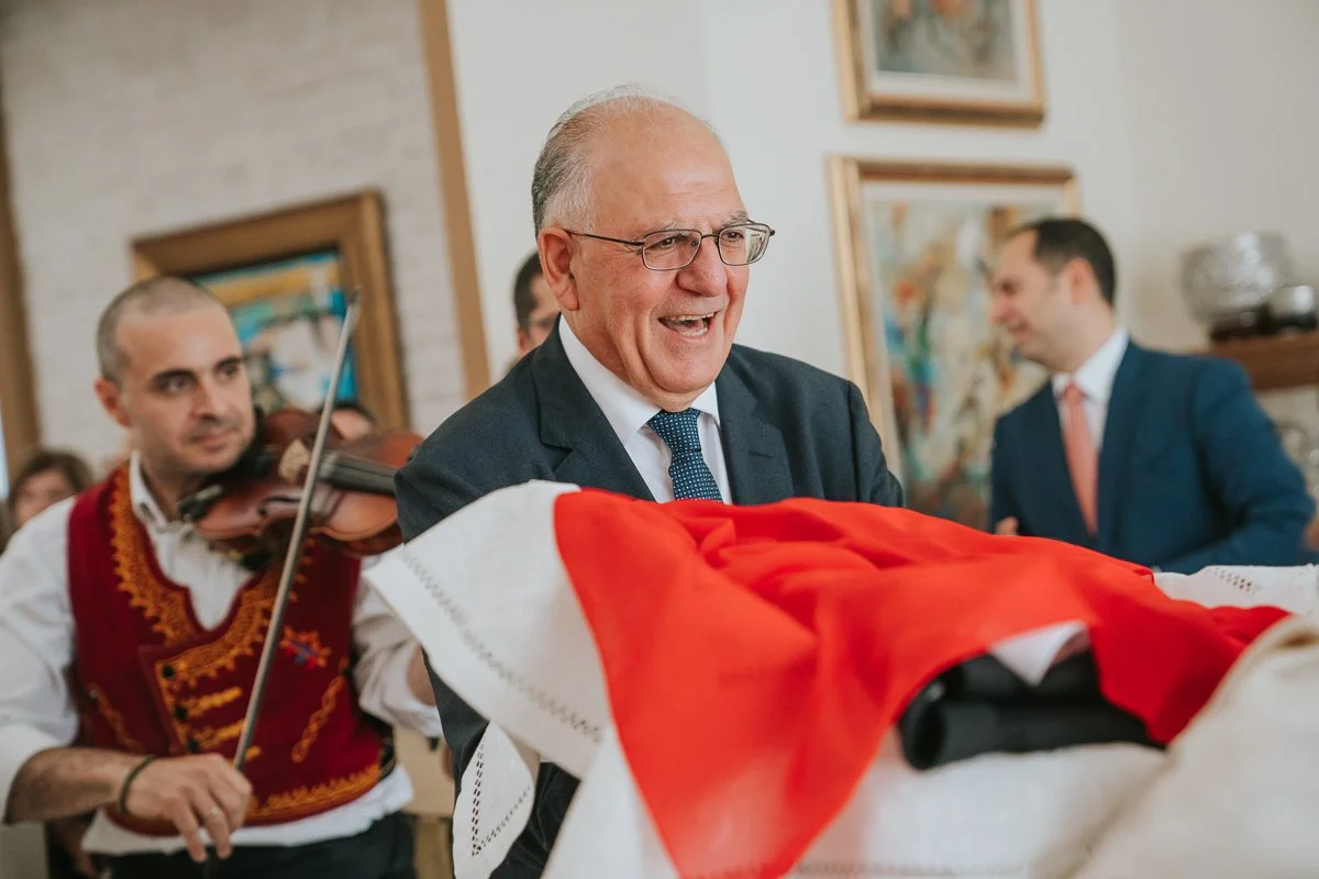  Traditional Greek Orthodox stolisma as the groom's father presents the wedding attire while live musicians perform during the pre-wedding celebrations. 
