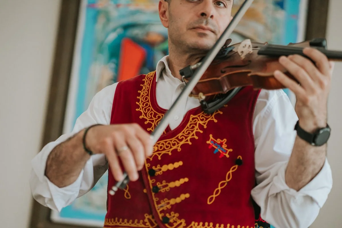  Musician playing traditional Greek music during a lively Orthodox stolisma, bringing atmosphere and energy to the wedding preparations.   