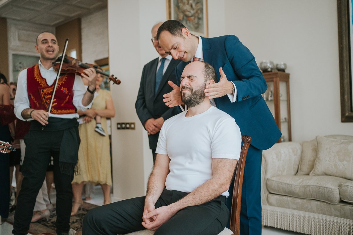  Traditional Greek Orthodox stolisma as the groom receives a slap on the face from his best man while live musicians perform during the pre-wedding celebrations. 