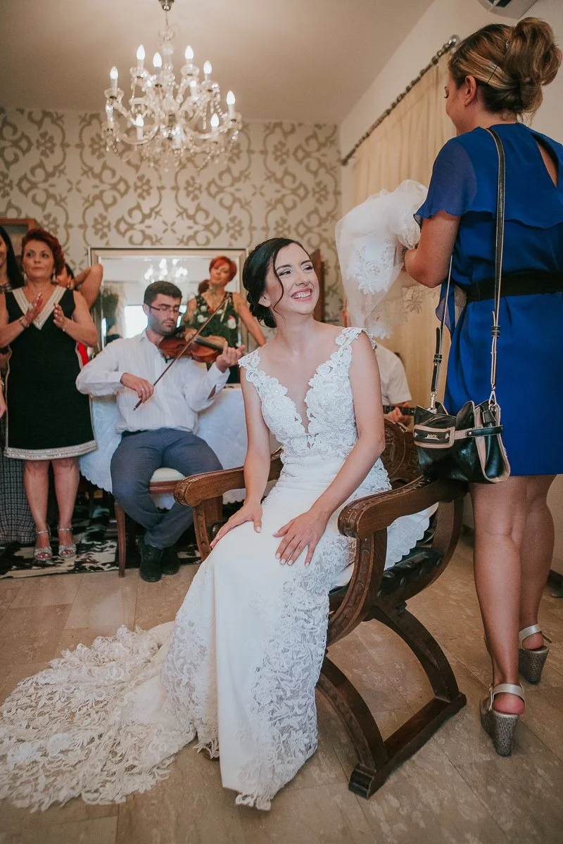  Bride sharing a joyful moment with family and musicians during a traditional Greek Orthodox stolisma before the wedding ceremony. 