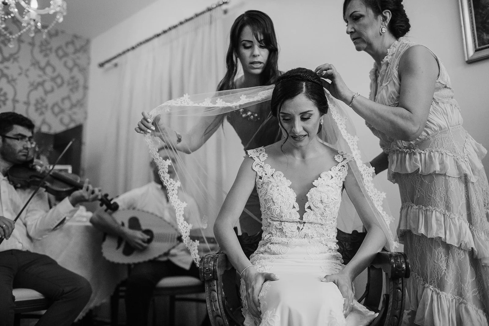  Bride's mother and bridesmaid placing the wedding veil during a traditional Greek Orthodox stolisma surrounded by family and live music. 
