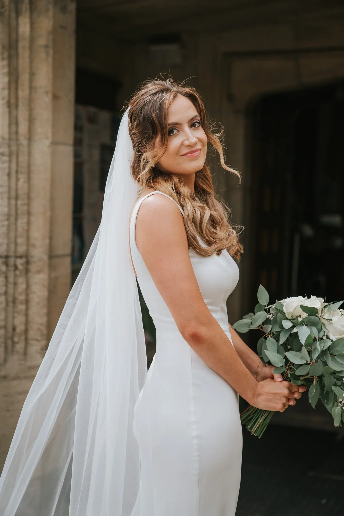  Natural bridal portrait outside a Greek church in London, with the bride holding her bouquet and veil flowing behind her after the wedding ceremony. 