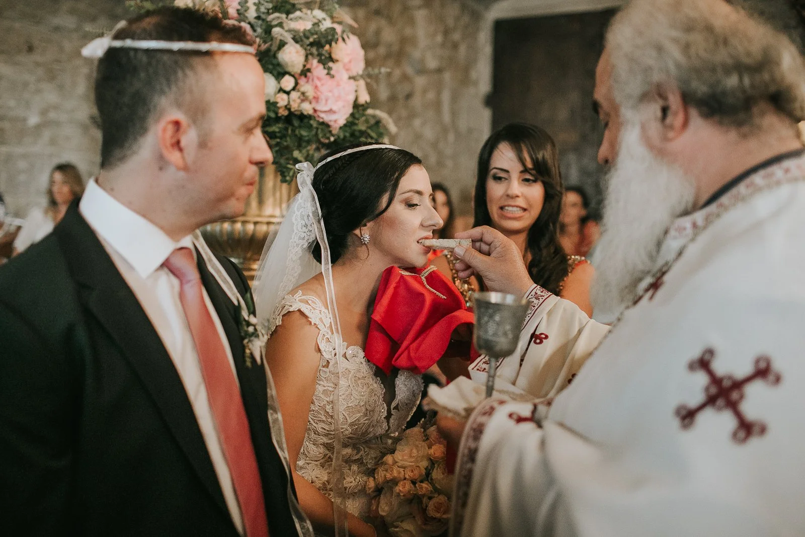  Bride receiving Holy Communion during a traditional Greek Orthodox wedding ceremony inside a beautifully decorated church. 