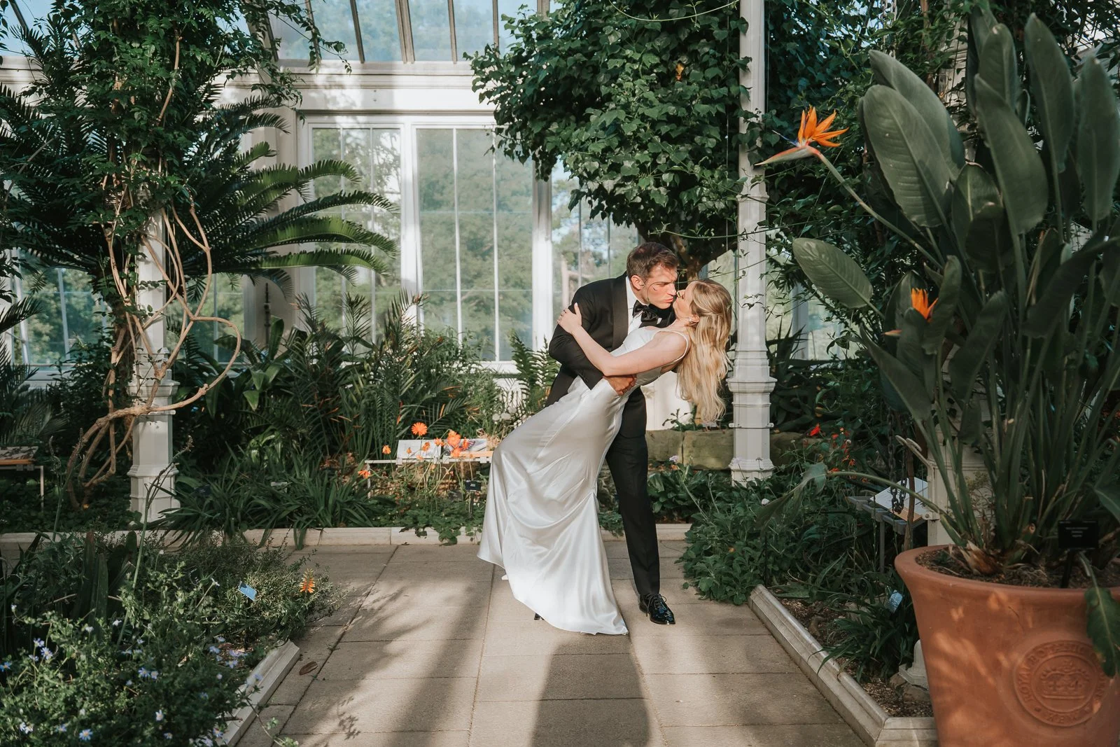 Bride and groom sharing a dramatic kiss beneath the glasshouse windows of the Temperate House, creating a timeless Kew Gardens wedding photograph. 