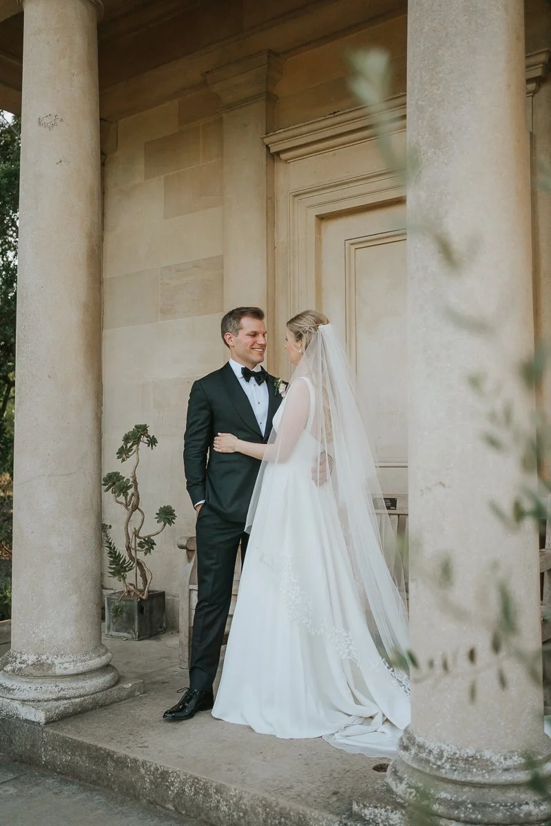  Romantic wedding portrait of a bride and groom standing beneath the stone columns of King William’s Temple, one of Kew Gardens’ most picturesque photo locations. 