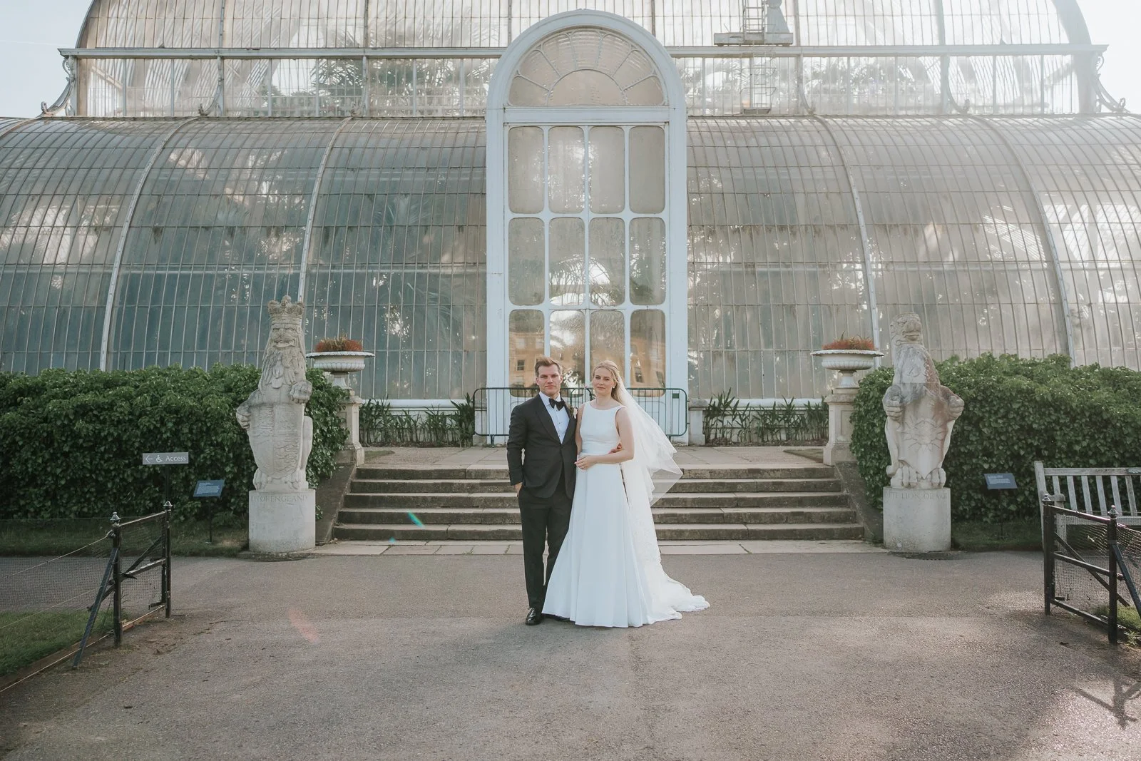  Newlyweds posing in front of The Palm House at Kew Gardens, with the iconic Victorian glasshouse providing a stunning backdrop for wedding photography. 
