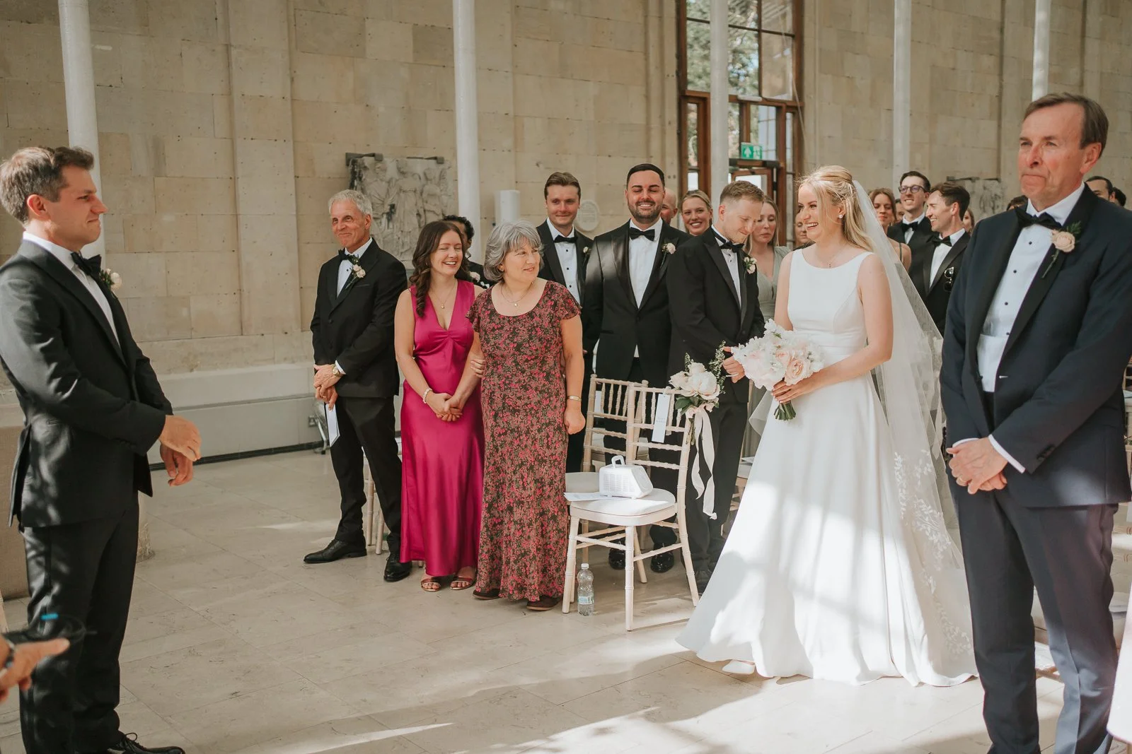  Bride making her entrance into the Nash Conservatory at Kew Gardens, greeted by smiling family and friends during the wedding ceremony. 