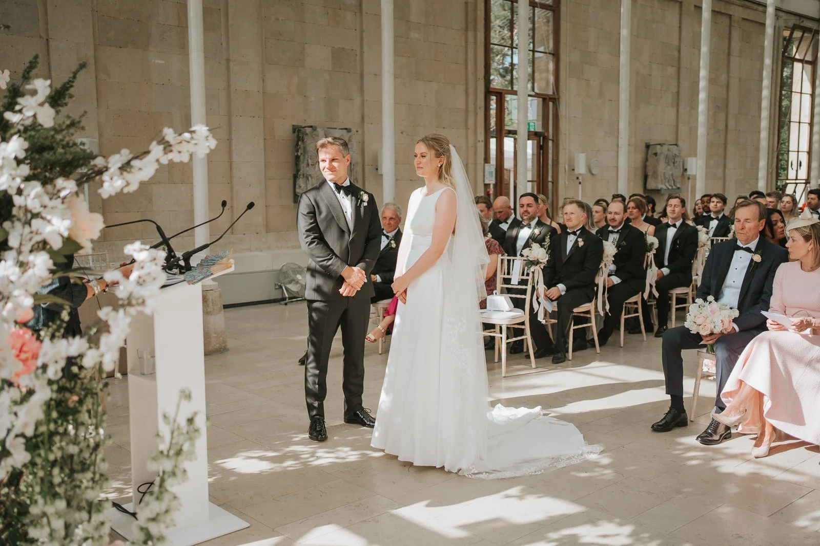  Wedding reading inside the Nash Conservatory at Kew Gardens, with the bride and groom standing together before their guests. 