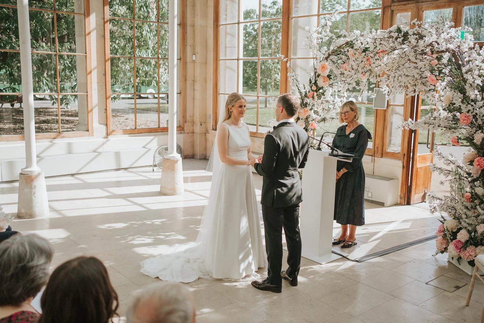  Bride and groom standing together during their wedding ceremony in the sunlit Nash Conservatory at Kew Gardens. 